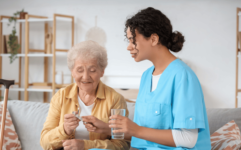 female nurse helping elderly woman open medication and holding a glass of water