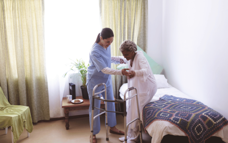female nurse helping elderly woman get our of bed in her own home